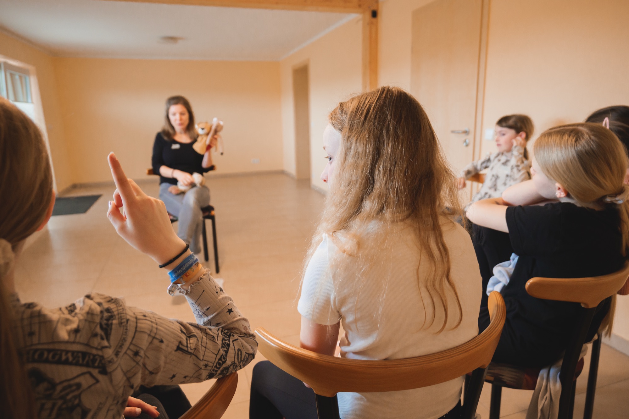 Sarah Veyel mit einer Puppe vor einer Gruppe Kinder, ein Kind hebt die Hand
